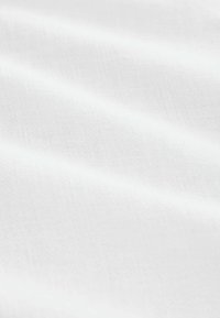 Weißer Stoff mit einer glatten Textur, der subtile Falten und ein feines Webmuster zeigt, was auf leichte und atmungsaktive Eigenschaften hindeutet.
