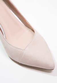 Escarpin beige en daim à bout pointu avec une texture lisse et un talon bas incurvé. Intérieur doté d'une doublure beige et de détails de couture minimaux.