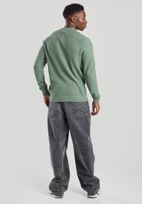 Green textured long-sleeve shirt with a crew neck, paired with loose, faded black denim pants featuring a back pocket design.