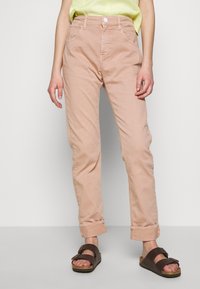 Vaaleanpunaiset puuvillapantsit, tapered-fit, etutaskut, käännetyt lahkeet, yhdistettynä ruskeisiin sandaaleihin, joissa on säädettävät hihnat ja korkkipohja.