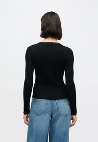 Μαύρο μακρυμάνικο κορμάκι με ριγέ υφή, λαιμόκοψη με κυματιστό τελείωμα και εφαρμοστή γραμμή, σε συνδυασμό με ανοιχτό μπλε τζιν παντελόνι με φαρδιά πόδια.