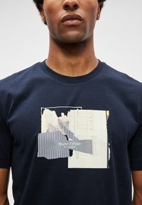 T-shirt de algodão azul marinho com uma estampagem gráfica apresentando várias texturas, incluindo riscas e formas abstratas, exibindo "Marc O'Polo."