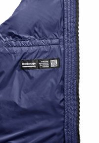 De binnenkant van de marineblauwe pufferjack heeft een ritszak, een label met een QR-code en een gladde, textuur nylon stof.