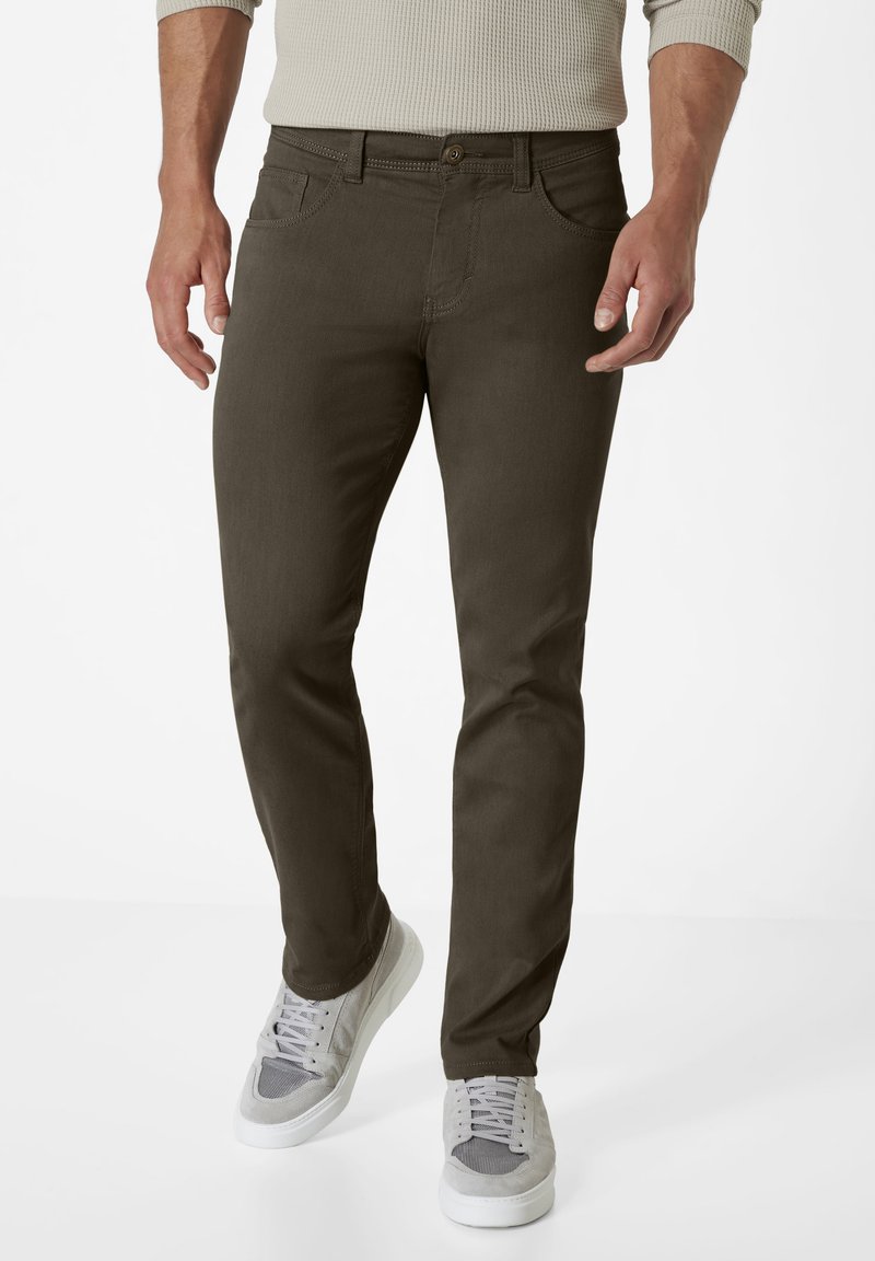 Men's dark olive green pants made of sturdy fabric, featuring a slim fit, five-pocket design, and a classic button fly. Paired with grey sneakers.