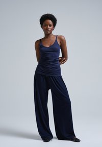 Navy tank top with thin straps, ruched detail, paired with loose-fitting, wide-leg navy pants. Soft fabric texture and relaxed design.