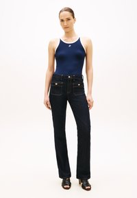 Μπλε σκούρο ριμπ αμάνικο τοπ με άσπρη επένδυση, σε συνδυασμό με σκούρο ντένιμ παντελόνι καμπάνα με δύο μπροστινές τσέπες και διακοσμητικά κουμπιά. Μαύρα πέδιλα με τακούνι.