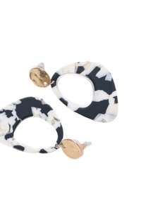 Orecchini marmorizzati in bianco e nero con un design a ritaglio ovale, caratterizzati da un accento circolare dorato e una finitura opaca.