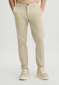 Chinos beige de corte entallado hechos de una tela ligera, con una textura suave, bolsillos frontales y cierre de botón. Adecuados para un uso casual.