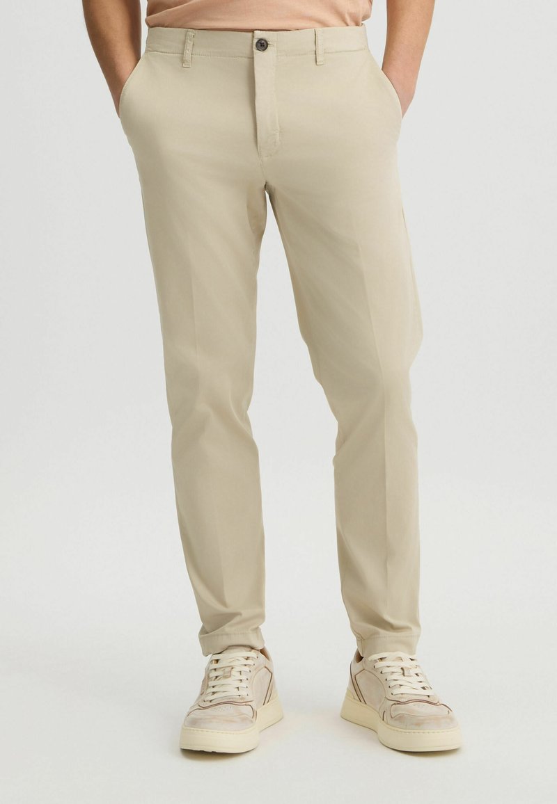 Chinos beige de corte entallado hechos de una tela ligera, con una textura suave, bolsillos frontales y cierre de botón. Adecuados para un uso casual.