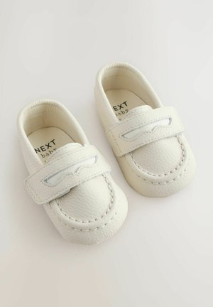 Valged beebijalatsid, mis on valmistatud tekstureeritud nahast, varustatud õmmeldud detailidega rihmaga ja pehme voodriga. Brändi nimi on sees nähtav.