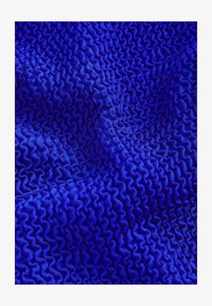 Tessuto blu testurizzato con un motivo ondulato, caratterizzato da creste affilate e linee fluide e morbide. Il materiale sembra sintetico ed elastico.