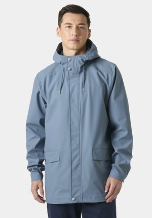 Hombre con chaqueta impermeable con capucha azul claro, con bolsillos de botones a presión y cordones ajustables, sobre un fondo liso.
