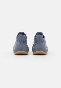 Widok z tyłu niebieskich sneakersów z teksturowaną cholewką, zaokrąglonym obcasem i jasnobrązową gumową podeszwą, z płynnym przejściem od pięty do palców.
