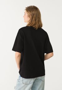 Sort oversized t-shirt lavet af bomuld, med korte ærmer og rund halsudskæring. Bæres med lyseblå slidte jeans.