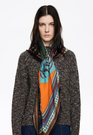 Zijde sjaal met turquoise, oranje en gestileerde accenten, elegant om de nek gedrapeerd, gestyled met een gestructureerde bruine sweater.