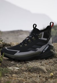 Μαύρο και γκρι πεζοπορικό παπούτσι Adidas Terrex με κορδόνια σε βραχώδες έδαφος, σχεδιασμένο για εξωτερική χρήση σε μονοπάτια και δύσκολες συνθήκες.