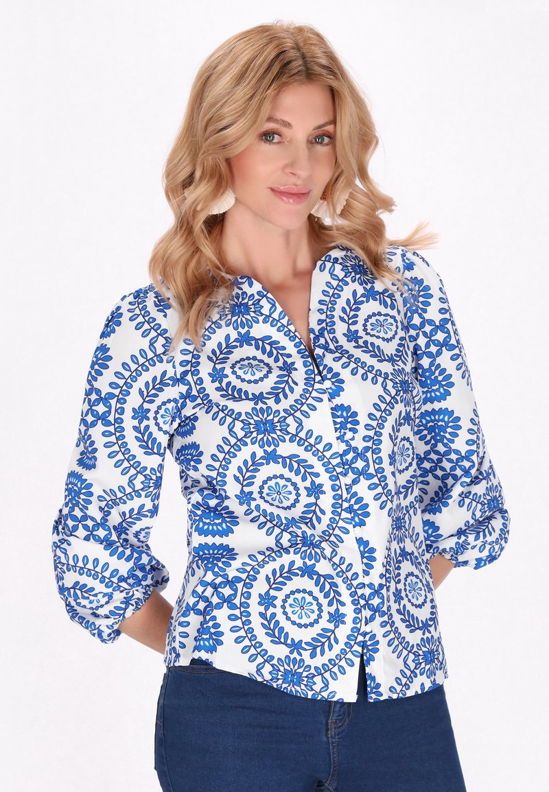Camicia bianca con motivo floreale blu, design con bottoni e maniche a tre quarti. Tessuto morbido con una leggera lucentezza.