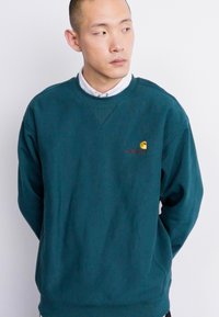 Teal crewneck sweatshirts laget av bomull med ribbede mansjetter og hem. Har en liten brodert logo på brystet.