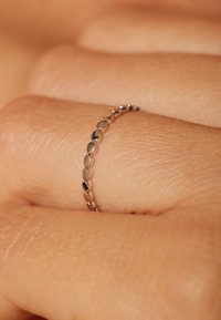 Thin silver band ring featuring an alternating pattern of oval and round links, resting on a textured human finger.