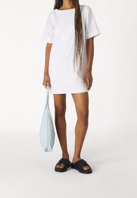 Vestido corto de lino blanco con escote cuadrado, combinado con sandalias planas negras y un bolso tote azul claro.