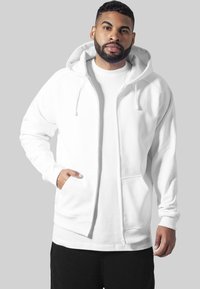 Witte rits hoodie van katoenmix, met een capuchon met trekkoord, voordoelen en geribbelde boorden, gedragen over een wit shirt.