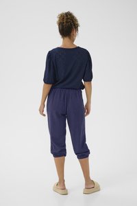 Top blu navy con dettagli a occhio di pernice, maniche a sbuffo; pantaloni abbinati fino al polpaccio in una consistenza morbida. Design con schiena scoperta, sandali piatti casual.