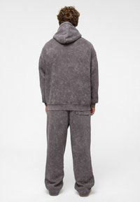 Grijze katoenen hoodie met een gestructureerde, onregelmatige afwerking, gecombineerd met bijpassende losse broek. Voorzien van een grote capuchon en zijzakken.