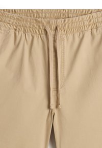 Beige shorts med elastisk talje, justerbar snor, glat stofstruktur og syninger langs sømmene.