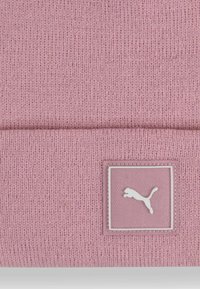 Gorra de punto rosa con vuelta, textura suave y una etiqueta de marca con un logo blanco sobre un fondo cuadrado.