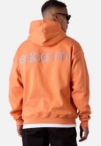 Hoodie orange avec un grand logo texturé "estéem" en gris au dos, doté d'une capuche avec cordon de serrage et de poignets et ourlet côtelés.