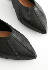 Fekete bőrcipők hegyes orral, varrott varratokkal és sima textúrával. Az alakja elegáns és jól megformált.