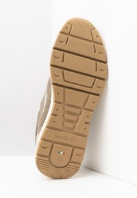 Baskets en suède beige avec une semelle en caoutchouc à motif, un talon renforcé et un design minimaliste avec des détails de marque sur la semelle.