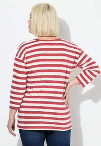 Rood-wit gestreepte lange mouwen top, met een ontspannen pasvorm en een ronde zoom, gedragen met donkerblauwe jeans, met zicht op de achterkant.