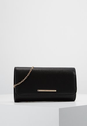 Czarna, teksturowana kopertówka z cienkim złotym łańcuszkiem i małym, poziomym złotym paskiem na przedniej klapie, leżąca na białej powierzchni.