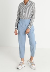 Randig skjorta i svart och vitt; ljusblå high-waisted byxor; vita sneakers med grå och orange detaljer.