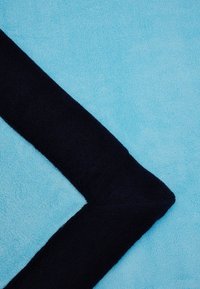 Turkise håndklæde med en mørk navy kant. Stoffet er blødt og tekstureret, med et hjørnedesign der fremhæver de kontrasterende farver.