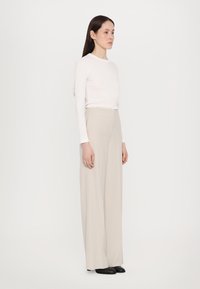 Beige wijde broek van zachte stof, gecombineerd met een langemouwige witte top. De outfit heeft een minimalistisch ontwerp en neutrale kleuren.