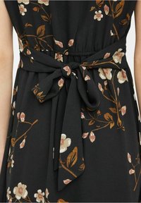 Svart tygdress med blommönster i nyanser av rosa och brunt. Har en åtstramad midja och en knuten rosett som dekoration på baksidan.