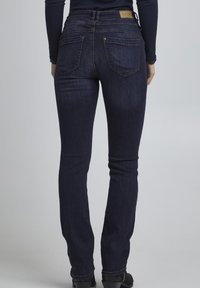Tmavě modré skinny džíny vyrobené z denimu, s vysokým pasem, zadními kapsami se švy a jemným strukturovaným povrchem.