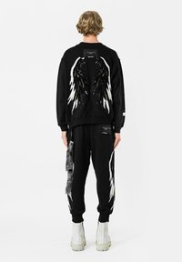 Sudadera negra con diseño de alas que presenta lentejuelas y acentos en blanco contrastantes, combinada con pantalones de chándal negros a juego y botas blancas hasta el tobillo.