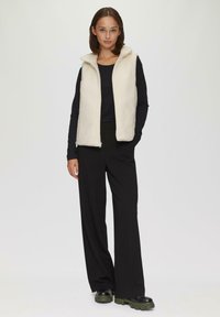 Kurtka polarowa w kolorze kremowym z zamkiem z przodu i kapturem. Połączona z czarną bluzką z długim rękawem i szerokimi czarnymi spodniami. Masywne czarne buty dopełniają całość.