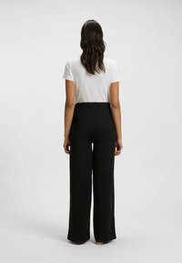 Zwarte wijde broek met een hoge elastische tailleband, gemaakt van een gladde stof. Gecombineerd met een plain wit T-shirt.