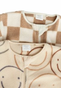 Zwei Babyschlafsäcke, einer mit einem braun-beigen Karomuster, der andere mit Smileys, beide aus weichem Fleece-Material.