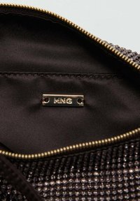 Pochette en tissu noir avec un extérieur brillant et texturé ornée de petites perles. Détail de fermeture éclair dorée et une étiquette intérieure portant l'inscription "MNG".
