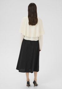 Tej könnyű, krémszínű pulóver, réteges kialakítással, fekete, laza szoknyával párosítva. A fekete magassarkú cipők teszik teljessé az öltözetet.