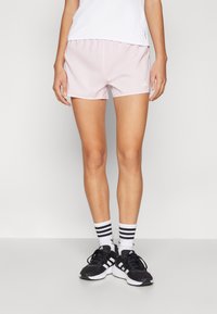 Rosa treningsshorts med en glatt tekstur og elastisk midje, parret med svarte joggesko og hvitstripete sokker.