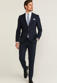 Costume marine avec une coupe ajustée, comprenant une veste à un bouton, des revers crantés et un pantalon à plis plats. Comprend une cravate bleu clair et un mouchoir de poche.