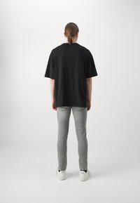 Svart oversized t-shirt med korta ärmar, tillsammans med ljusgrå slim-fit jeans och vita sneakers. Enkelt design utan mönster eller logotyper.