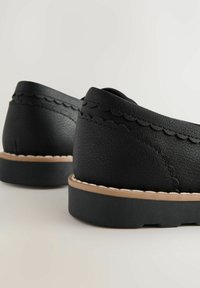 Sorte læder sko med en struktureret finish, bølgemønster omkring kraven og en kontrasterende tan gummisål.