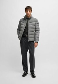 Giacca a vento grigia con yoke a maglia testurizzata, chiusura con zip e tasche laterali, abbinata a pantaloni grigio scuro e scarpe nere.